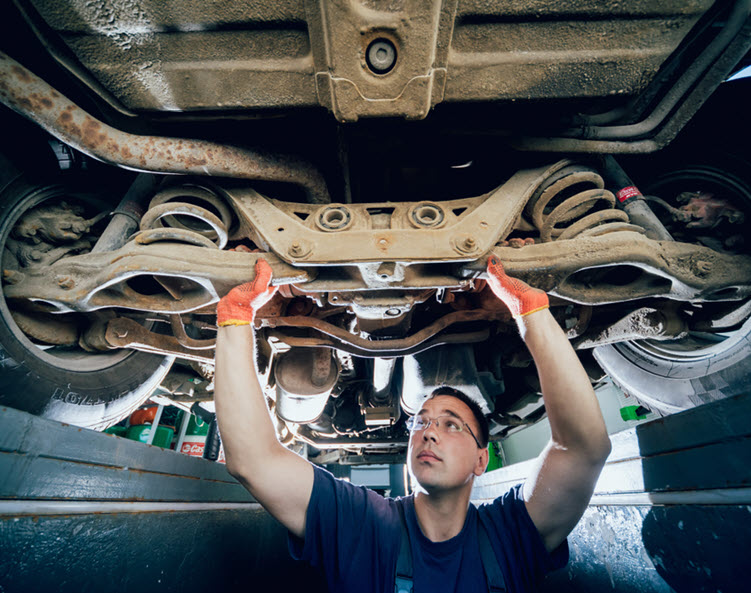 A repair technician examines an undercarriage from a pit under a car