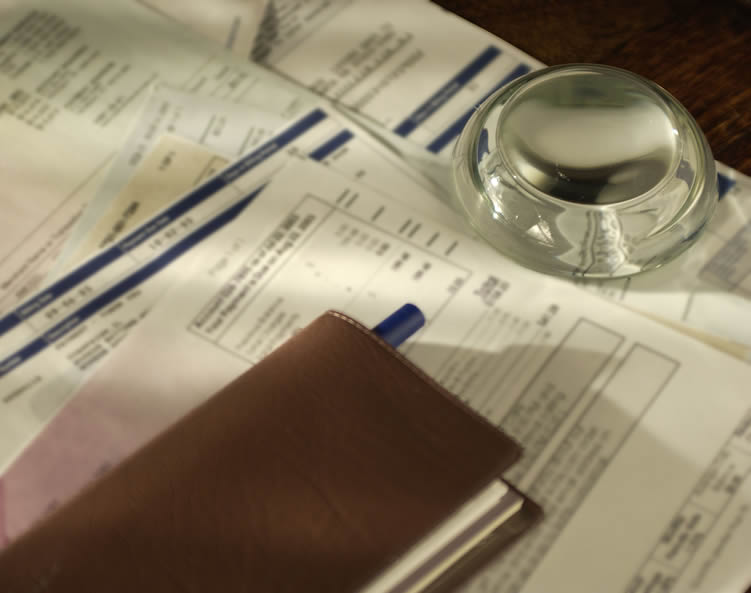 A clear glass paperweight and a check book sit on top of financial papers