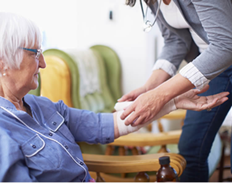 A nurse wraps a bandage around the arm of an elderly patient