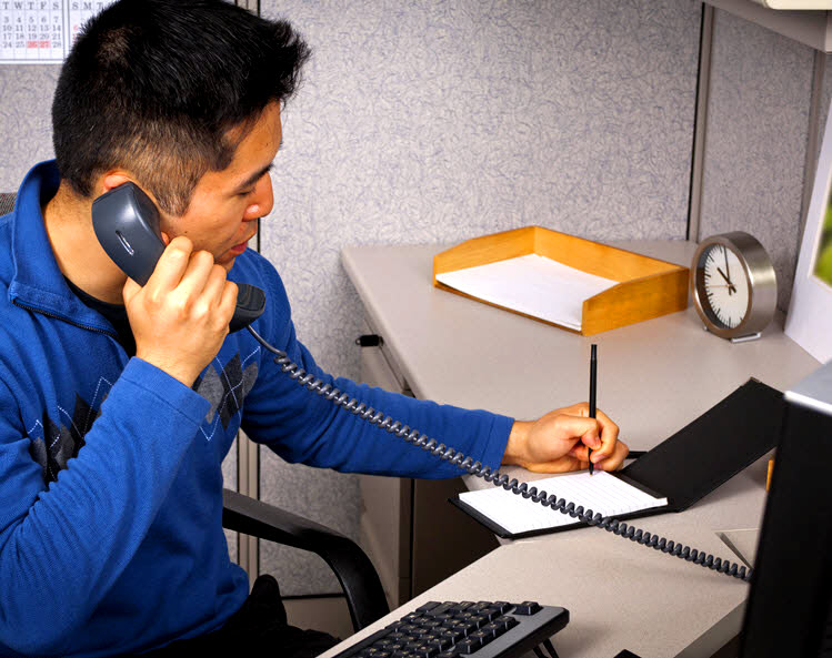 Office worker talks on a phone while writing notes